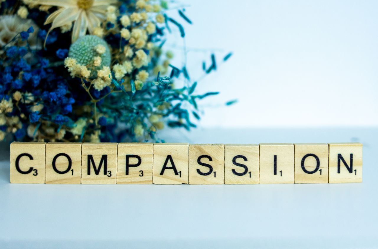 Scrabble tiles spelling 'compassion' with vibrant floral background.