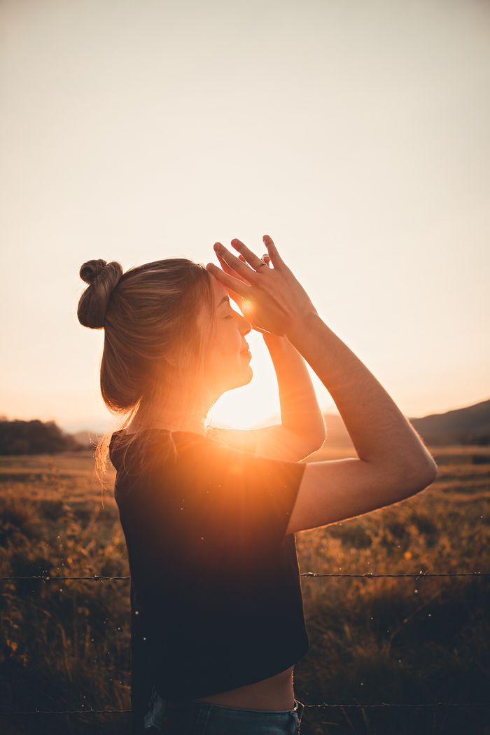 Silhouette of a woman in a field at sunset, hands clasped, enjoying the warm sun rays.